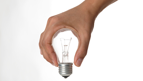 Hand holding light bulb in front of a white background.
