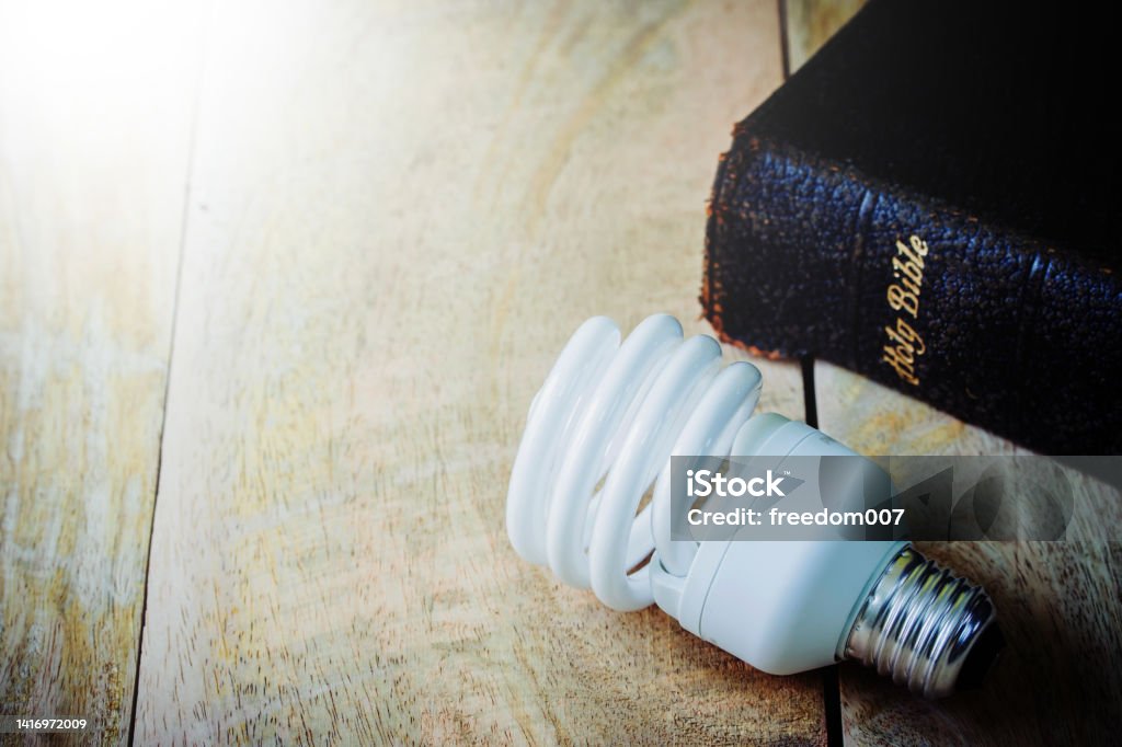 Close up of the light bulb and the holy bible Close up of the light bulb and the holy bible on wooden table background, christian devotional or bible study concept with copy space Bible Stock Photo