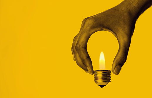 Hand holding light bulb in front of a yellow background.