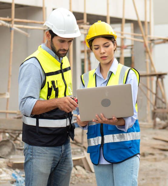 The engineer man and female architect discuss housing development project at construction site using laptop computer. Engineer man and female architect wear safety helmets discuss housing development project at construction site using laptop computer. Contractor manager inspecting house building estate infrastructure estate worker stock pictures, royalty-free photos & images