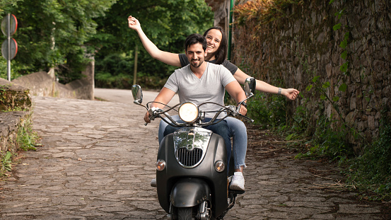 Young and carefree couple learning to drive a scooter on a road. Young man is teaching hipster girl to ride a motorcycle.