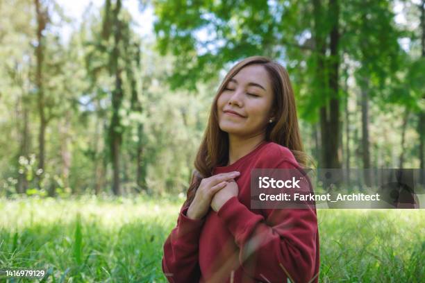 Portrait Image Of A Young Woman With Closed Eyes Putting Hands On Her Chest In The Park Stock Photo - Download Image Now