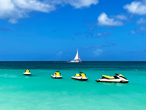 Personal watercraft lined-up in the Caribbean sea, off the coast of Aruba. A Sailboat in the background.