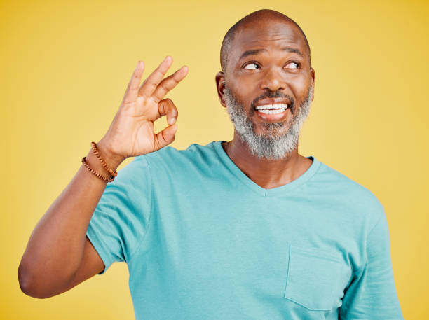 istock Mature african american man smiling while making an okay gesture with his hand against a yellow studio background. Expressing that everything is perfect. Showing support 1416983084