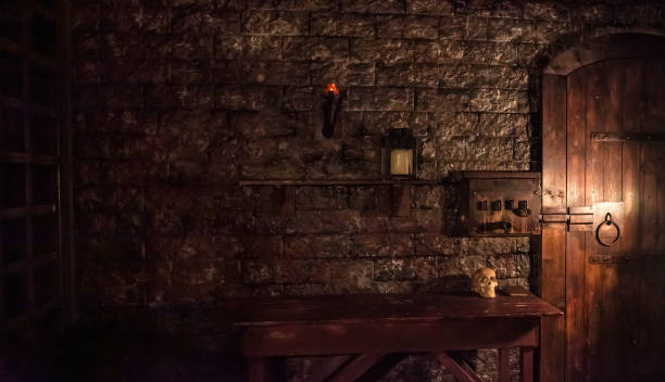 고대 돌담에 대한 테이블 위에 큰 나무 문과 두개골이있는 중세 방의 신비로운 어두운 인테리어의 배경. 할로윈 휴가를위한 놀라운 배경. 복사 공간, 텍스트 장소 - castle indoors domestic room spooky 뉴스 사진 이미지