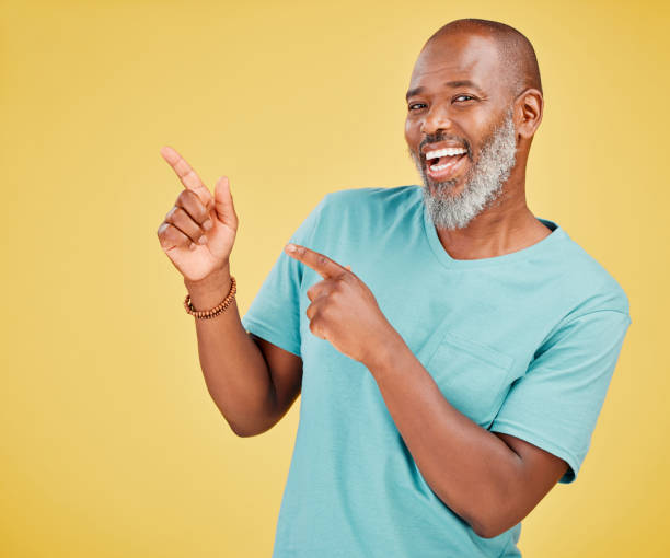 istock Mature african american man with a beard smiling and making a hand gesture pointing with his fingers standing against a yellow studio background. Happy, smiling, showing 1416992530
