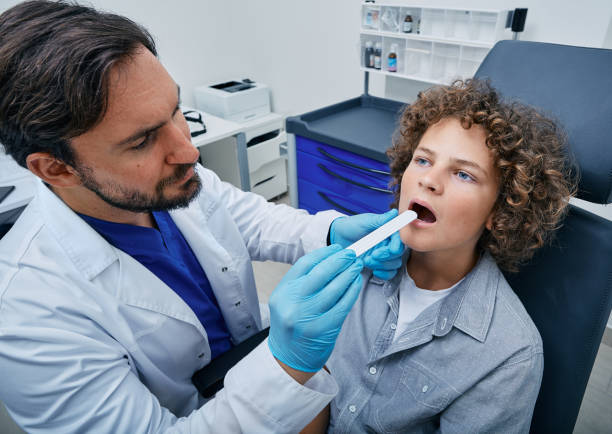 doctor using inspection spatula to examine curly boy's throat. male child at pediatrician appointment - doctor patient male tongue depressor imagens e fotografias de stock