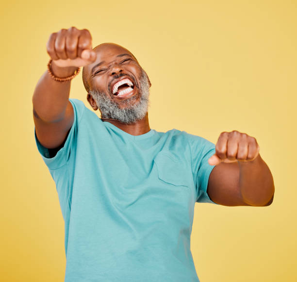 istock A mature african man looking ecstatic while while celebrating by making a fist pump gesture with his hands and cheering against a yellow studio background. Success and Celebrations infuse life with passion and purpose 1416996472