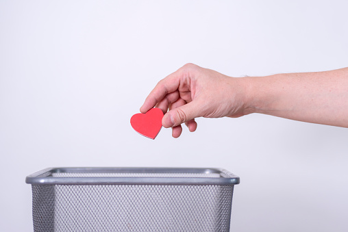 Handmade wooden heart tossed in the trash for recycling and disposal. Gray background, selective focus, copy space.