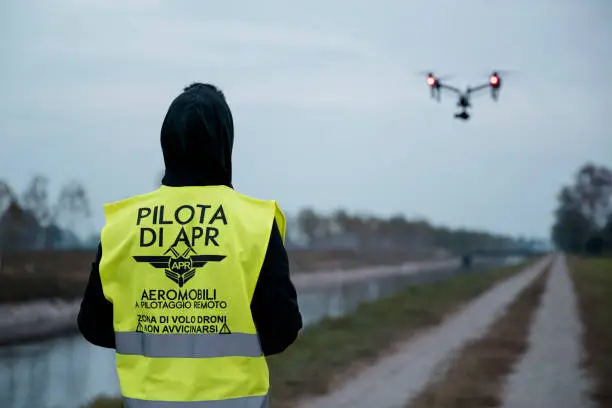 Pilot operating the drone by remote control wearing high visibility vest (Translated by Italian: "APR Pilot. Aircraft remote controlled. Flight zone, do not get close.")