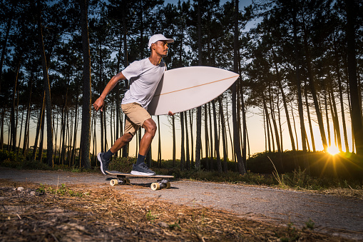 Surf skater rolling by the pine forest at sunset with his surfboard in Maceda, Ovar - Portugal.