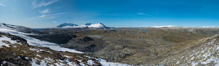 Wide Panoramic view from Krossbu on glacier Smorstabbreen, snow-capped mountains and blue lakes in Jotunheimen National Park, Western Norway.
