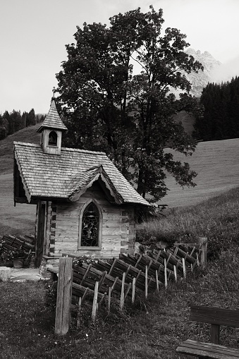 A vertical grayscale shot of a small alpine chapel in the Hutten district of Leogang, Austria.