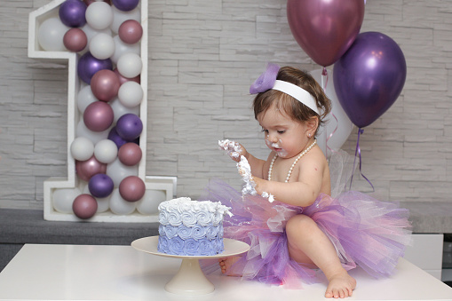A one-year-old girl tried her first birthday cake. Surrounded by balloon decorations and the number 1 decorated by her parents