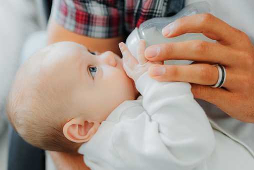 Close-up of baby holding and drinking milk from bottle in father's arms