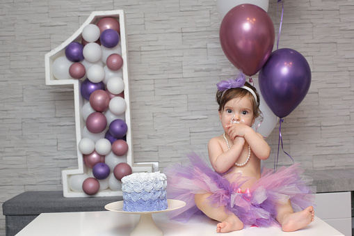 A child with an appetite eats a birthday cake for his first birthday. Festive decor made of balloons