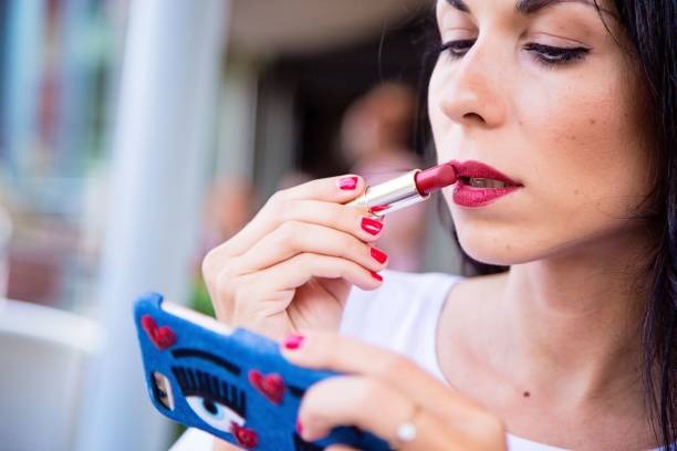 istock Beautiful young woman applying lipstick on her lips using her smart phone as mirror 1417015254