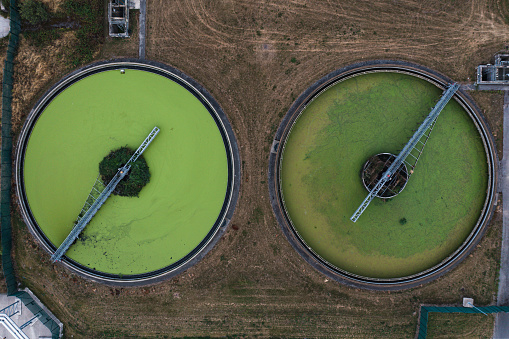 An aerial view directly above a waste water treatment works with circular storage tanks filtering wastewater with green algae for drinking water