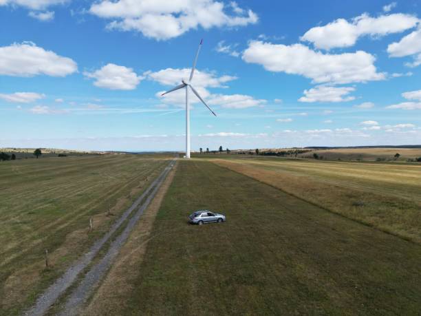 istock Green field with a silver car and a wind turbine 1417020058