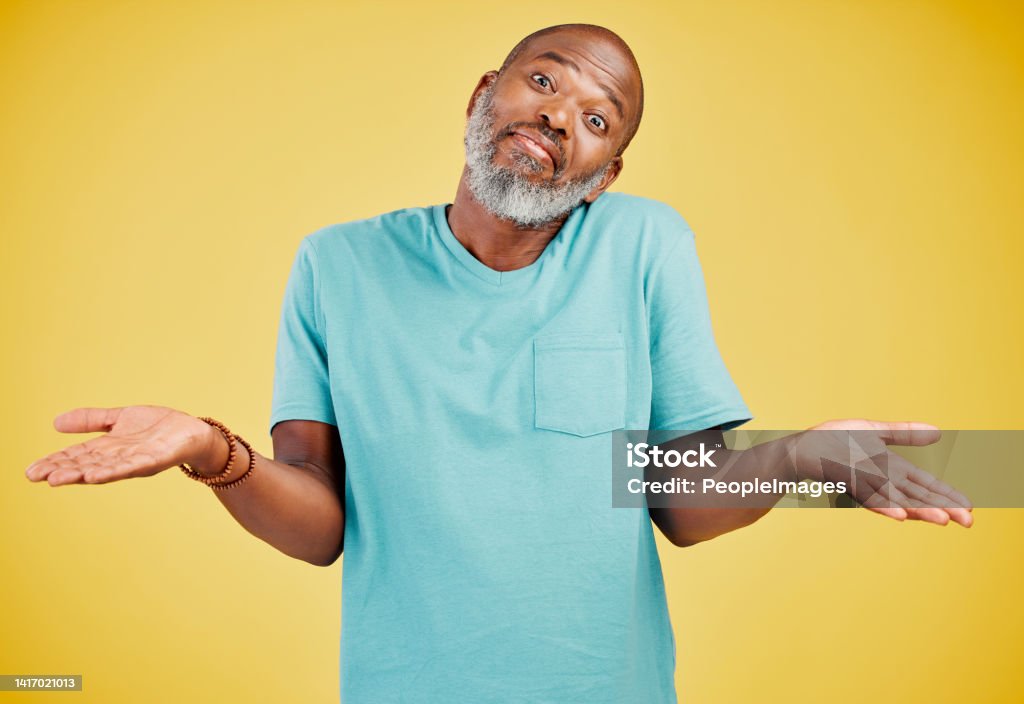 Portrait of a mature african american man smiling and making a gesture of not knowing something while smiling against a yellow studio background. Black african man looking quirky. Sometimes you don't know what surprises might be waiting for you Men Stock Photo