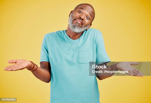 Portrait Of A Mature African American Man Smiling And Making A Gesture Of Not Knowing Something While Smiling Against A Yellow Studio Background Black African Man Looking Quirky Sometimes You Dont Know What Surprises Might Be Waiting For You Stock Photo - Download Image Now