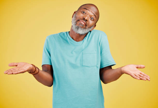 portrait of a mature african american man smiling and making a gesture of not knowing something while smiling against a yellow studio background. black african man looking quirky. sometimes you don't know what surprises might be waiting for you - blank expression head and shoulders horizontal studio shot imagens e fotografias de stock