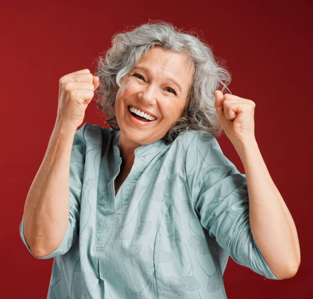 Celebrating, cheering and winning with a happy, smiling and excited senior female posing in studio against a red background. Portrait of a cheerful, wow and positive mature female with a fist gesture Celebrating, cheering and winning with a happy, smiling and excited senior female posing in studio against a red background. Portrait of a cheerful, wow and positive mature female with a fist gesture punching the air stock pictures, royalty-free photos & images