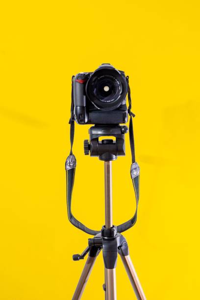 istock Camera on a tripod isolated on bright yellow background 1417024413