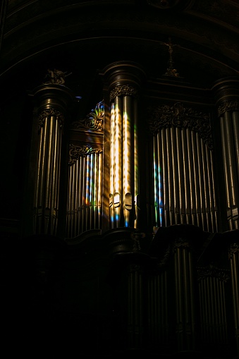 A vertical shot of beautiful organ pipes with a rainbow reflection on them in dark