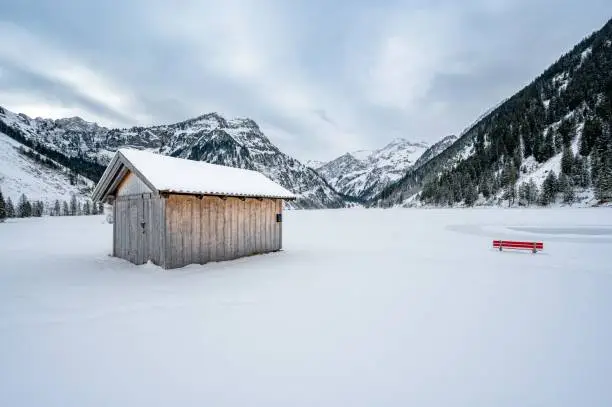 A glacier lake Vilsalpsee, a hut, and a red bench in the background of the Alps covered in snow, Austria