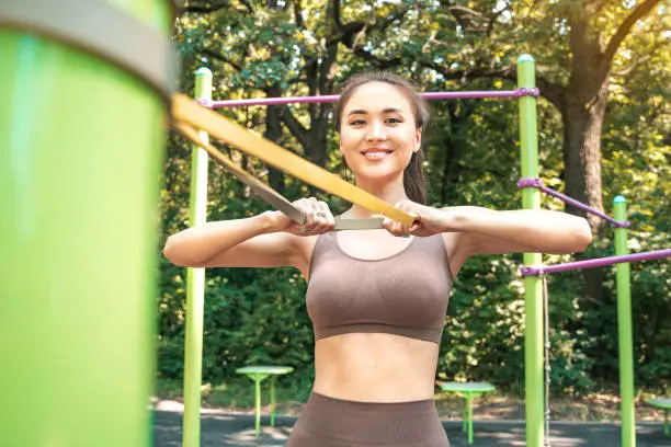 Young asian woman working with resistance band in the street sports ground.