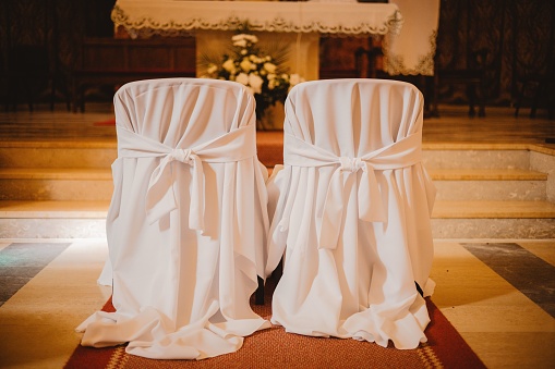 A close-up shot of two wedding chairs decorated with white fabrics in a church