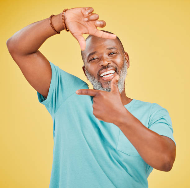 portret szczęśliwego dojrzałego afrykańczyka wykonującego gest kadru dłońmi na żółtym tle studyjnym. życie jest pełne szczęśliwych chwil i powinniśmy spróbować uchwycić je klatka po klatce. - focus finger frame frame human hand zdjęcia i obrazy z banku zdjęć