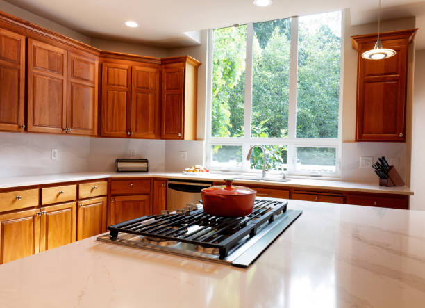 Contemporary upscale home kitchen interior with wood cabinets, gas stove, stainless steel vent hood, concrete countertops, glass tile backsplash and view windows