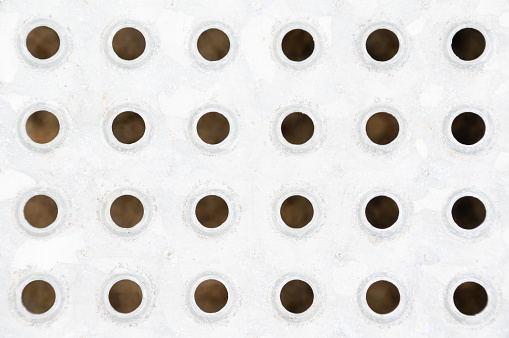 Perforated white metal plate with pattern of circular holes displaying symmetry and repetition