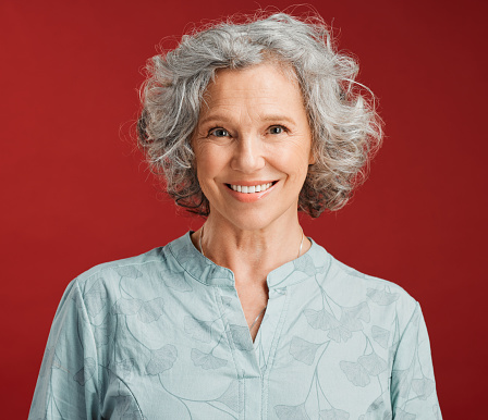 Portrait of senior, happy and cheerful woman standing against a red studio background. Mature woman with healthy, white and clean teeth showing oral and dental health with a friendly bright smile