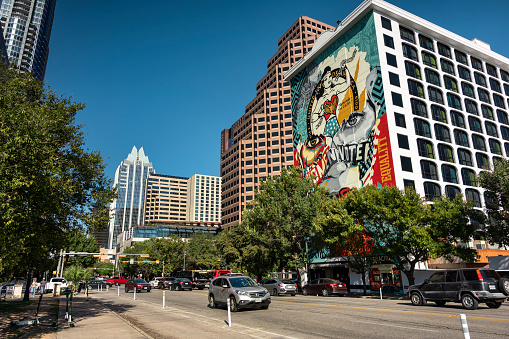Austin, Texas, USA - November 15, 2021:  People and cars move along the modern buildings of Congress Avenue in the downtown core of Austin Texas USA.  With a strong economic focus on government and education, since the 1990s, Austin has become a center for technology and business.