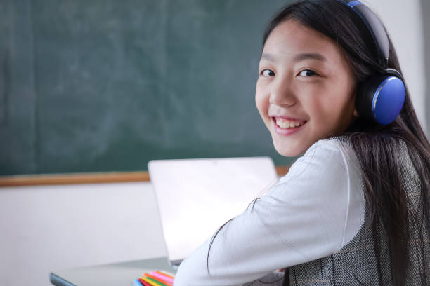 istock Happy student wearing headphones using computer laptop in the classroom, Student sitting in front of blackboard, School day concept 1417043775