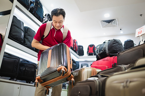 Mid adult Asian man buying luggage suitcase at retail shop. Black Friday, Fashion and Beauty, Business Finance and Industry, Travel & Holiday Vacations, Financial Freedom Concepts.
