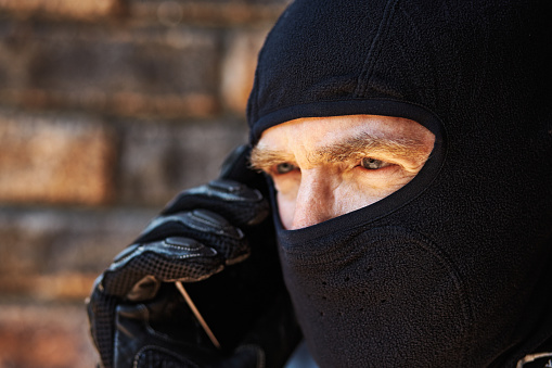 Scary-looking man wearing ski mask listens to his mobile phone.