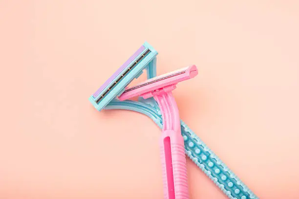 Disposable blue and pink razors on a pastel pink background