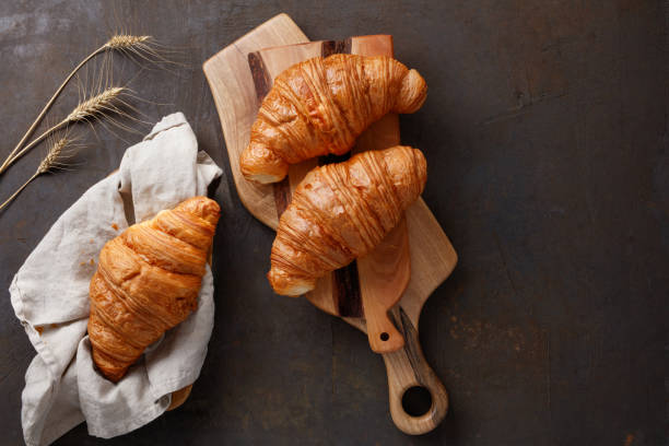 istock Board with tasty croissants on dark table with spikelets, close up. 1417046155