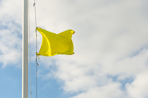 Yellow small flag on flagpole with cloudy sky