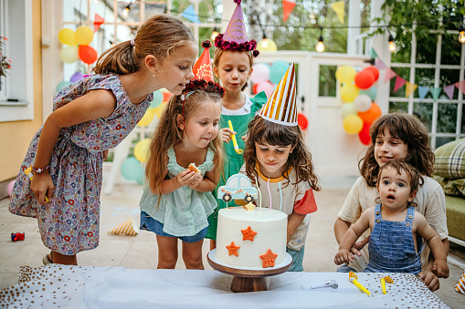 Children with cake standing around table on birthday party in garden in summer.