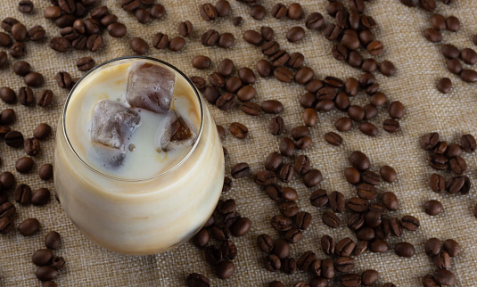 A glass with coffee ice cubes and milk on the surface with scattered coffee beans. Cold summer drink.