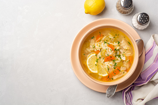 Italian lemon chicken orzo soup in bowl on concrete background. Top view, copy space.