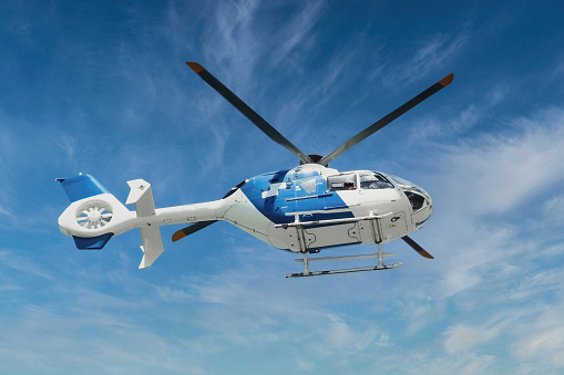 Blue and white air ambulance rescue helicopter flying mid-air against a blue sky background