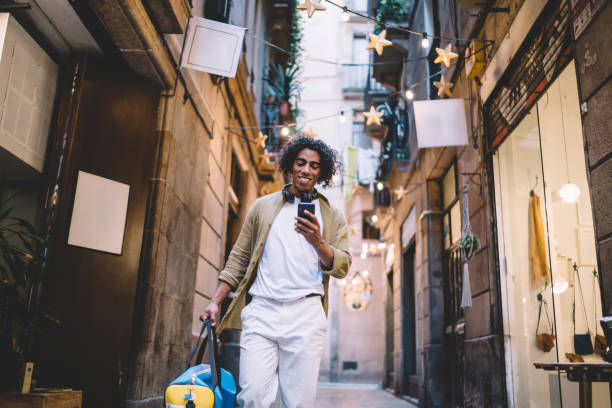 istock Happy ethnic young man with suitcase browsing smartphone on sidewalk 1417056869
