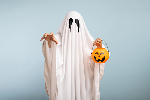 Concepto de Halloween. Un fantasma blanco con ojos negros, hecho de una sábana con canasta de calabaza para dulces sobre fondo azul photo