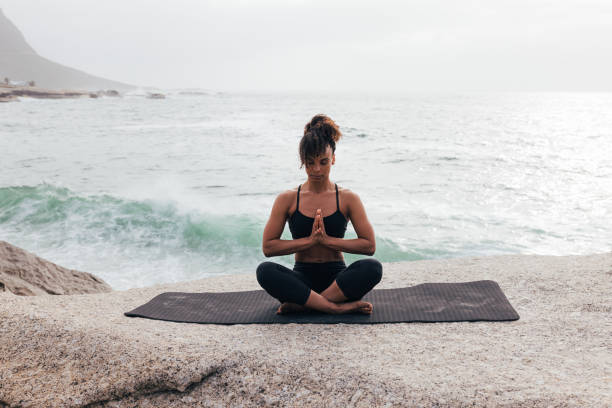 istock Fit woman with crossed legs meditating while sitting on mat by ocean 1417062361